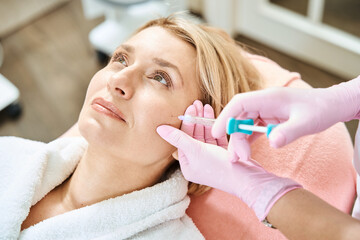 Cropped female cosmetologist doing face beauty injection with syringe of woman