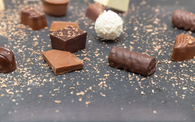Chocolates and pieces of milk chocolate on a stone black plate