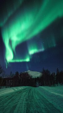Strong and beautiful aurora dancing on a windy winter night, above a mountain viewed from a road.