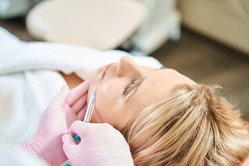 Partial female beautician doing face beauty injection of woman in beauty salon