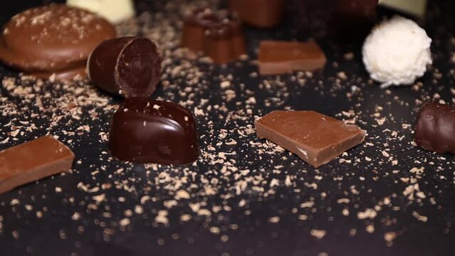 Chocolates, pieces of milk chocolate on a stone black plate and hand taking a chocolate candy.