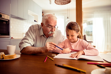 Grandfather helping granddaughter with drawing at home