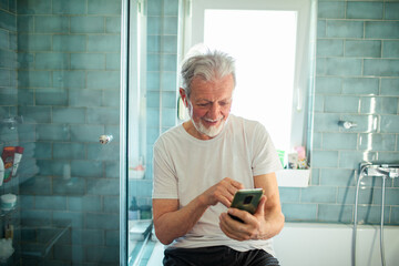 Smiling senior man using smartphone in the bathroom