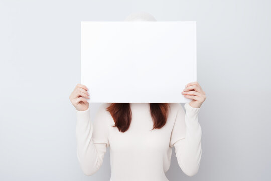 Junge Frau h&auml;lt ein leeres wei&szlig;es Schild vor sich, Plakat mit Textfreiraum f&uuml;r Werbung und Botschaften