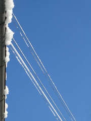Blue sky and wintertime, roof gutter and power cables covered by white iced snow