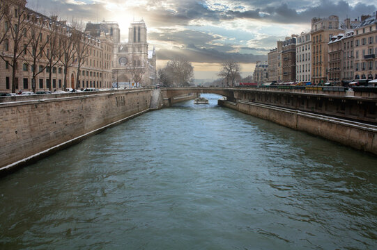 the sun between the towers of notre dame while a boat can be seen on the seine river