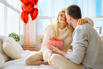 Young man giving present to his girlfriend at home. Beautiful young couple at home celebrating...