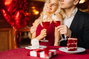 Young couple  celebrating  Valentine's Day with glass of red wine in the restaurant. Relationship, surprise and love concept.
