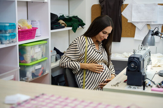 Pregnant craftswoman in the workshop works at a sewing machine