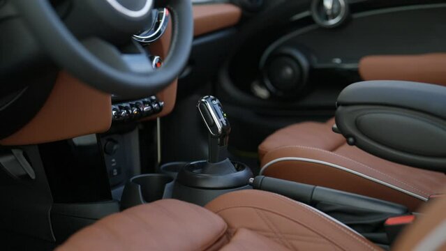 Interior of city sports car Mini Cooper S Convertible with front seats in brown leather and dashboard details. Steering wheel and speed shifter of classic vehicle