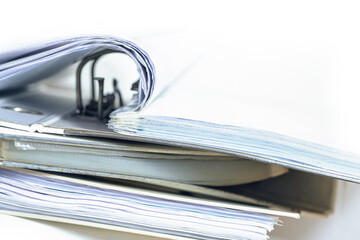 Part of an open ring binder with many documents on a stack of more file folders, business and...