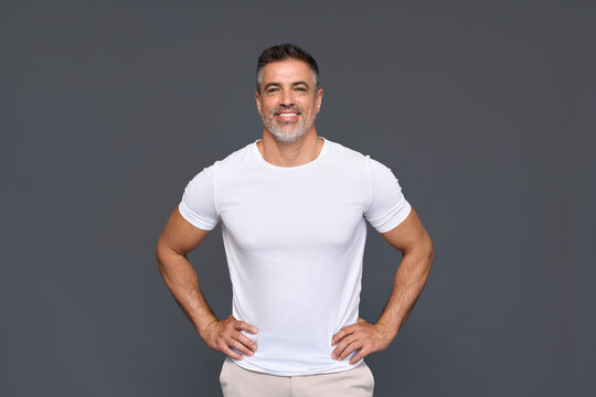 Happy confident handsome fit sporty healthy mature older man, middle aged sportsman athlete or personal trainer wearing white t-shirt standing isolated on gray background advertising gym. Portrait