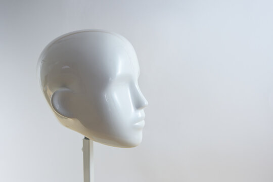 White Neutral Head Of A Mannequin Figure In Minimalist Style On A Metal Stand Against A Light Beige Gray Background, Copy Space