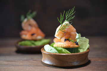 Party snack from shrimp, salmon, caviar and dill garnish in small wooden bowls on a dark rustic...