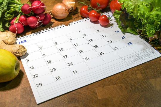 Calendar with month of January surrounded by fresh vegetables and fruits on a wooden table, new year goals to eat healthy food and lose weight, copy space, selected focus