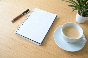 Blank spiral notepad, coffee cup, pen and a plant on a desk made of bamboo wood, business or home office concept, mockup, copy space, selected focus