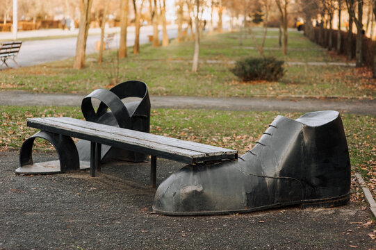 Architecture, a made antique metal painted bench in the form of shoes, sandals stands in the park in the autumn outdoors. Photography, retro building.