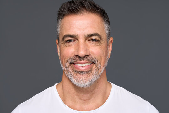 Happy confident handsome healthy mature older man, smiling middle aged male model wearing white t-shirt standing isolated on gray background advertising skin care and dental smile concept.