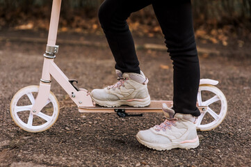 A girl, a child in sneakers rides on a pink scooter on the asphalt in the fall. Photography,...