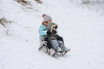 Fototapeta na wymiar A little boy with his sister's girl, happy children, a family, sitting together on a sled, going down a hill in the snow in winter. Photography, portrait, childhood concept, lifestyle.
