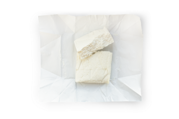 A briquette of fresh cottage cheese lies on a paper backing isolated on a transparent background.