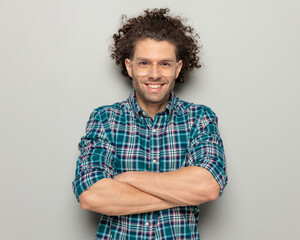 portrait of curly hair man with glasses smiling, looking forward and crossing arms