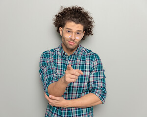 casual young guy with glasses pointing fingers forward and smiling - obrazy, fototapety, plakaty
