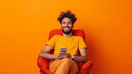 Full body young smiling happy Indian man he wears t-shirt casual clothes sit in bag chair use mobile cell phone type message isolated on orange red color background studio portrait. Lifestyle concept.