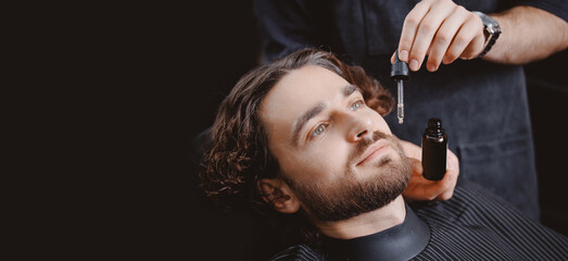 Barber use dropper with oil for beard of man in barbarshop. Concept banner spa care for men hair