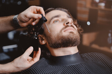 Barber applies oil with dropper for beard man in barbarshop.