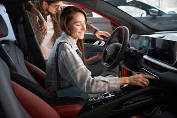 Man and woman testing car for buying choosing automobile in dealership