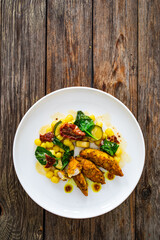 Fried chicken breast fillet with gnocchi and sun dried tomatoes on wooden table