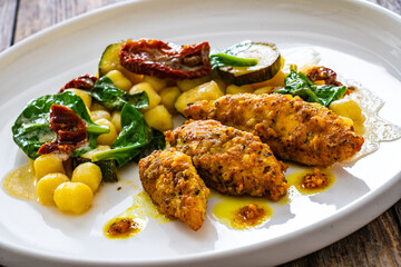 Fried chicken breast fillet with gnocchi and sun dried tomatoes on wooden table