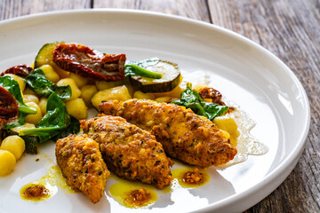 Fried chicken breast fillet with gnocchi and sun dried tomatoes on wooden table