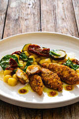 Fried chicken breast fillet with gnocchi and sun dried tomatoes on wooden table