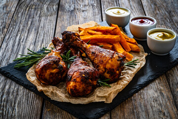 Roasted chicken drumsticks with French fries on wooden table