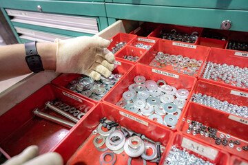 A worker selects and shows washers lying in a hardware box.