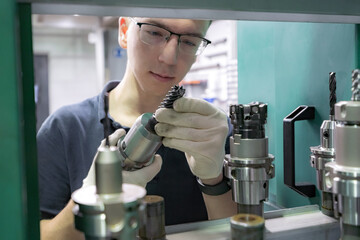 A working machine operator inspects a cutter for a CNC machine from a tool rack.