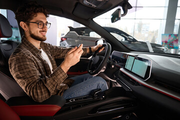 Man holding auto key sitting in automobile rejoicing car purchase in dealership