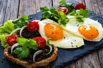 Breakfast - sunny side up egg, tapenade bruschetta and fresh vegetables on wooden table