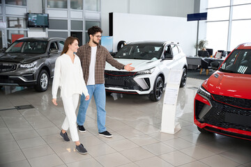 Man and woman choose car in auto salon thinking about automobile model and color