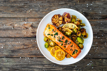 Fried salmon steak and garlic, brussels sprouts and lemon served on wooden table - obrazy, fototapety, plakaty
