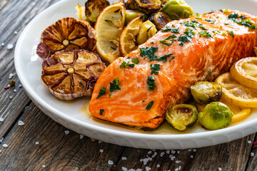 Fried salmon steak and garlic, brussels sprouts and lemon served on wooden table