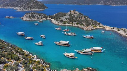 Excursion boats take a swimming break in Aquarium Bay Kekova in Turkey. Cinematic drone shot flying over a beautiful bay with turquoise water and tour boats. Many motorboats  - obrazy, fototapety, plakaty