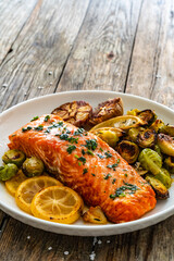 Fried salmon steak and garlic, brussels sprouts and lemon served on wooden table