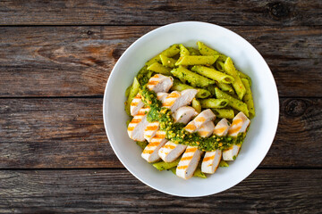 Penne with basil pesto sauce and grilled chicken breast on wooden table