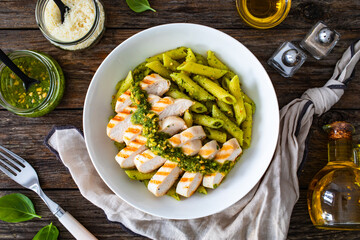 Penne with basil pesto sauce and grilled chicken breast on wooden table