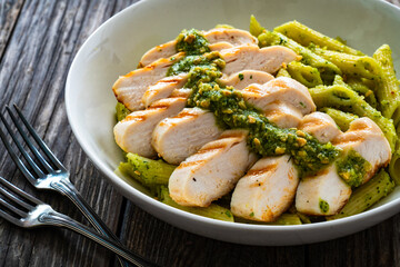Penne with basil pesto sauce and grilled chicken breast on wooden table