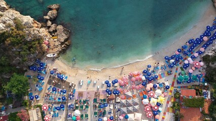 Top down view of sandy beach with turquoise sea water, colorful umbrellas and swimming people. Crashing waves in golden beach at Büyük Çakıl, Kaş resort in Turkey. Drone shot, Aerial view - obrazy, fototapety, plakaty