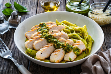 Penne with basil pesto sauce and grilled chicken breast on wooden table